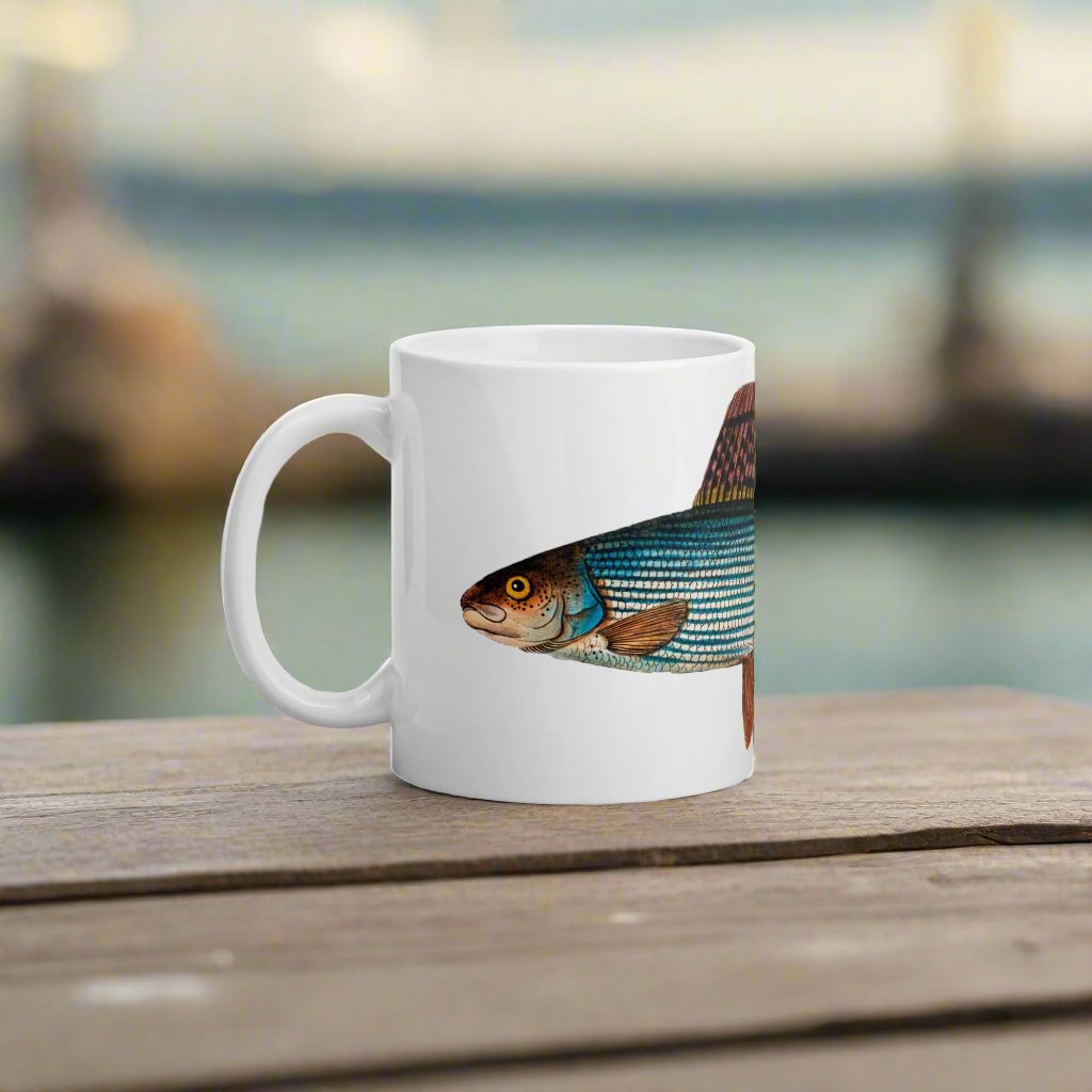 coffee mug with grayling trout design on a table with a waterfront view